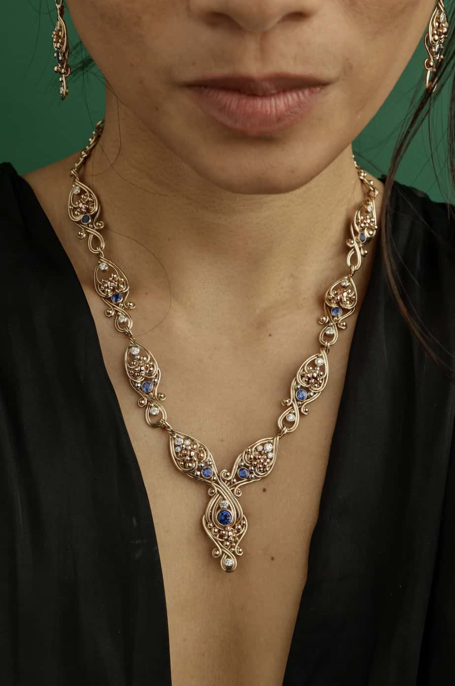 Close-up of a woman wearing an intricate gold and gemstone necklace.